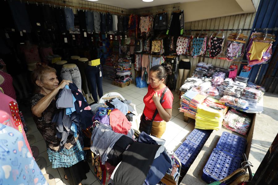 Una mujer muestra prendas de vestir a una clienta en una tienda de ropa, el 18 de abril de 2023, en el centro de San Salvador, El Salvador. EFE/Rodrigo Sura